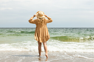 A girl in a dress walks on the beach in the summer.