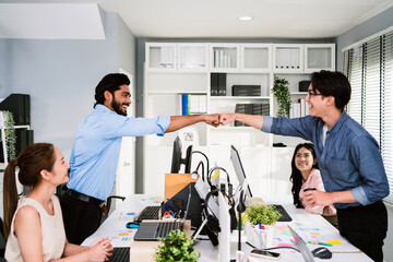 Cheerful Asian businessman partners making fist bump with a smile as a symbol of teamwork. Positive multi-ethnic business colleagues on diversity in the office. Collaboration concept - 770346242