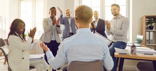 Business man sitting back speaking on a work meeting in office in front of a group of company employees discussing new project, applauding their leader celebrating success, making deal. Banner. - obrazy, fototapety, plakaty