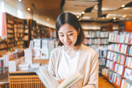 Portrait of young adult southeast asian woman reading book at bookstore shop