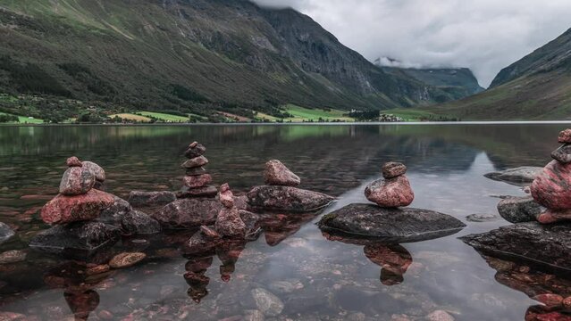 Peculiar stone cairns stand on the edge of the shallow lake, surrounded by mountains covered in forest.  A timelapse video.