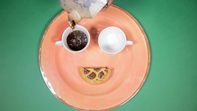 Overhead closeup shot: pouring coffee into two cups and accompanying them with a pastry snack, all arranged to form a happy face for the morning breakfast.