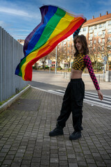 young man dressed in colorful and tight clothing waving the pride flag in the wind.