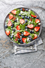 Fresh salad of spinach, strawberries and blueberries with cheese and pecans with honey dressing close-up in a plate on the table. Vertical top view from above