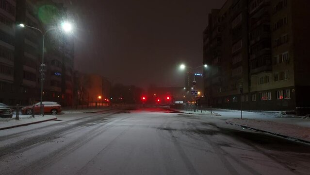 Snowfall and snow on the road on a city street at night against the backdrop of light from lanterns and buildings. Winter snowstorm and weather. Copy space for text, nighttime