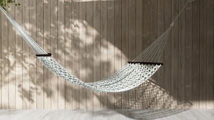 White rope hammock in dappled sunlight, tree leaf shadow on wood plank fence wall in garden at home...
