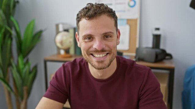 A cheerful young hispanic man with a beard smiling in a modern office setting, portraying a professional and approachable image.