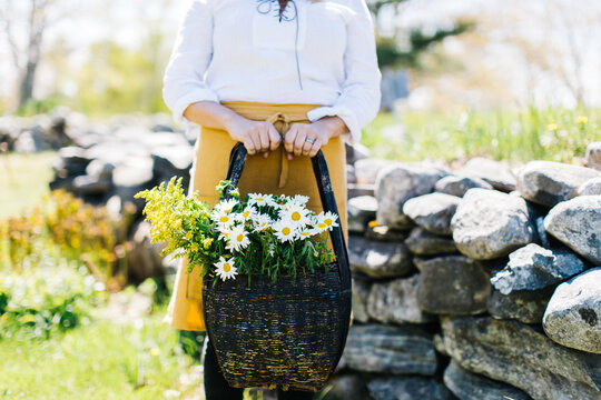 a young lady holding a basket full of daisies and goldenrod