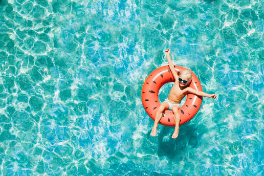 Drone aerial happy boy in pool in summer with watermelon floatie