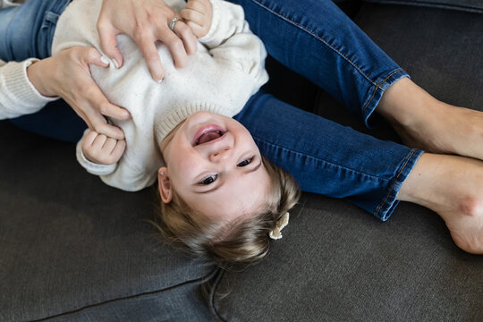 Overhead image of toddler girl laughing while mom tickles her