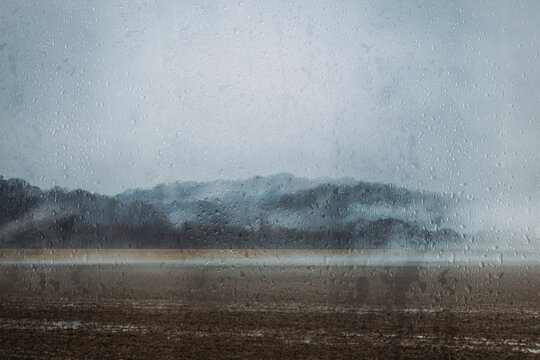 Gloomy landscape through raindrops on window on rainy day