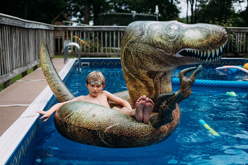 Child on dinosaur pool float in swimming pool