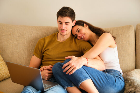Spanish couple watching a movie on the laptop while hugging.