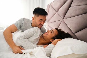 Multiracial romantic couple wake up together in bed during honeymoon.