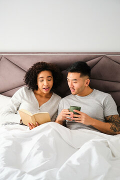 Multiracial couple learning languages with a book on bed together.