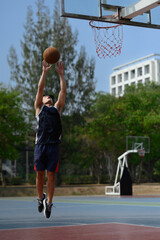 Athletic male training outdoor, playing basketball on sports court