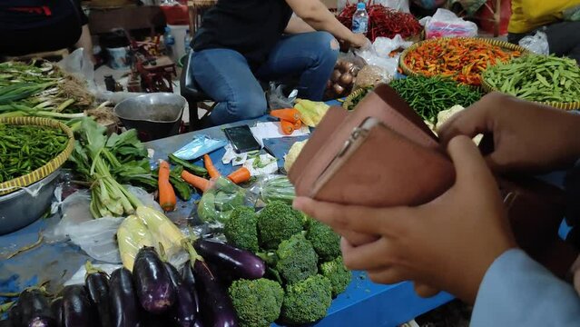 A woman counting money in her purse to buy vegetables at a traditional market