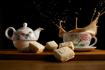 Taza de café con leche con tetera de flores y mariposas con fondo negro y salpicando unas pastas de té.