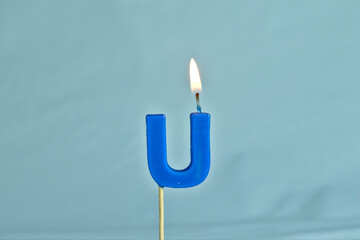 close up on a blue letter U birthday candle with fire on a white background.
