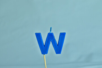 close up on a blue letter W birthday candle on a white background.
