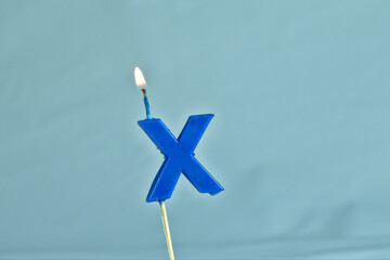 close up on a blue letter X birthday candle with fire on a white background.
