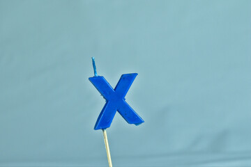 close up on a blue letter X birthday candle on a white background.
