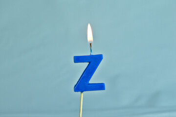 close up on a blue letter Z birthday candle with fire on a white background.
