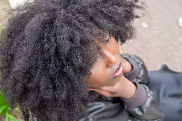 An intimate perspective of a young African American woman looking upwards, her voluminous afro...