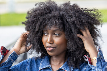 A close-up captures a stylish African American woman in a denim outfit, her natural hair framing...