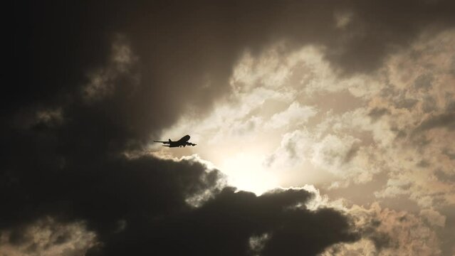 Silhouette of a plane flies through the clouds as the sun begins to set.