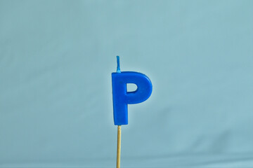 close up on a blue letter P birthday candle on a white background.
