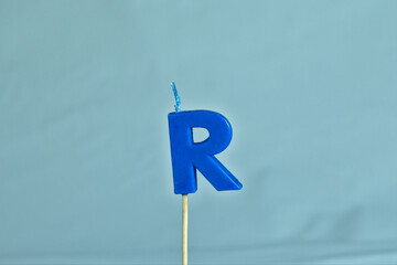 close up on a blue letter R birthday candle on a white background.
