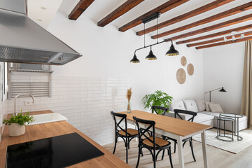 Horizontal shot of a loft-style kitchen-living room with a white wall of wooden beams with modern appliances, a dining table and a sofa corner in a relaxation area in a new apartment