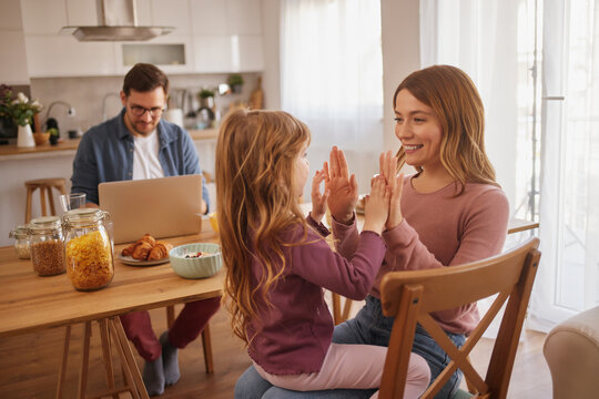 Happy mother and daughter clapping hands playfully in the kitchen