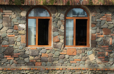 Fototapeta na wymiar new, modern Wall of building made from cobble stone with 2 two arched windows. exterior background. wooden antique vintage window frames in red brown brick wall. old fashion style