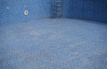 bottom of dirty leaking swimming pool removing water so the pool can be repaired. blue tiled of...