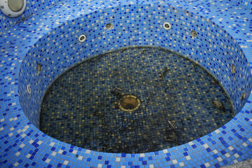 bottom of dirty leaking swimming pool removing water so the pool can be repaired. blue tiled of swimming pool with mosaic wall and bottom. after winter season