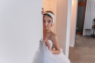 Close up portrait of ballerina with white tiara. Young dancer peeks from behind a wall, eyes...
