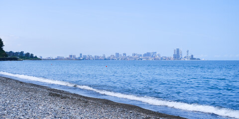 Batumi, Georgia - June 11, 2023. Black Sea pebble coast overlooking the city of Batumi. The water and sky are blue, sunny day. Travel and sea holiday concept. Panorama, copy space