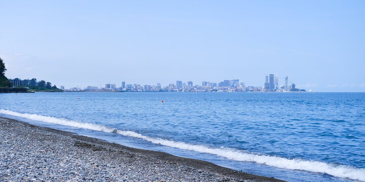 Batumi, Georgia - June 11, 2023. Black Sea pebble coast overlooking the city of Batumi. The water and sky are blue, sunny day. Travel and sea holiday concept. Panorama, copy space