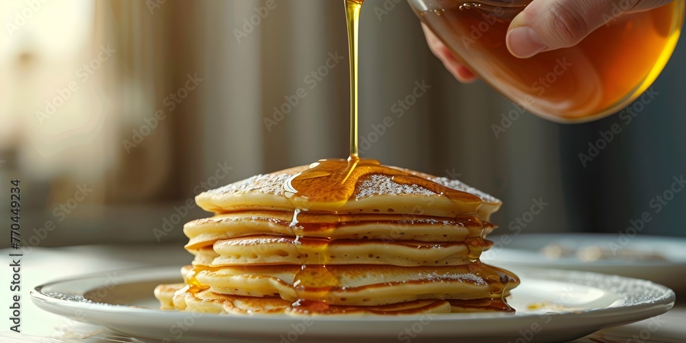 Poster a close up view of a hand pouring rich maple syrup over a stack of fluffy golden pancakes creating a