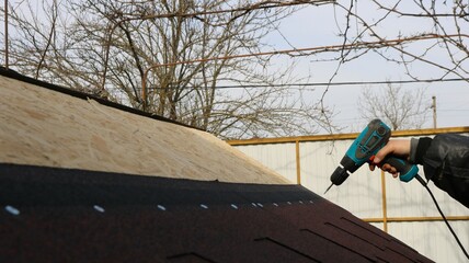 male hand with screwdriver tightening fasteners on wooden structure outdoors, assembly with...