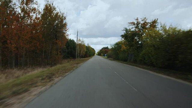 Auto is driving through Russian village along autumn trees in the evening. View through rear windshield windscreen of car in motion, back glass screen. Early fall. Cloudy weather. Background