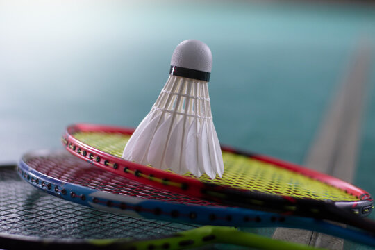 Cream white badminton shuttlecock and racket with neon light shading on green floor in indoor badminton court, blurred badminton court background, copy space.	