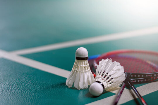 Cream white badminton shuttlecock and racket with neon light shading on green floor in indoor badminton court, blurred badminton court background, copy space.	