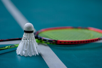 Cream white badminton shuttlecock and racket with neon light shading on green floor in indoor badminton court, blurred badminton court background, copy space.	