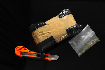 Smuggling, drug trafficking. Packages with narcotics and utility knife on black surface, flat lay