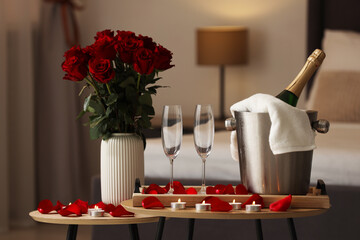 Honeymoon. Sparkling wine, glasses and bouquet of roses on wooden table in room