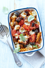 Baked pasta with cherry tomatoes, olives and mozzarella cheese. Bright wooden background. Top view.