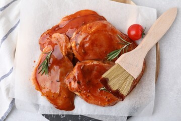 Raw marinated meat, rosemary, tomato and basting brush on light table, top view